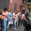 A Venezuelan soldier stands guard next to people forming a line to try to buy cornmeal flour and margarine at a pharmacy in Caracas